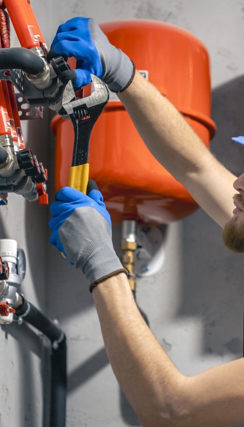 A man installs a heating system in a house and checks the pipes with a wrench. Adjusting heating valves in a residential building. A plumbing and heating technician works.